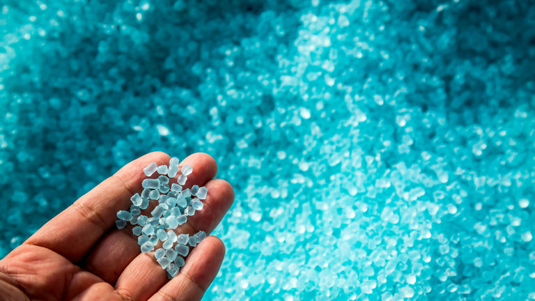 A hand hold or touching plastic pellets , plastic polymer dye granules color clear blue